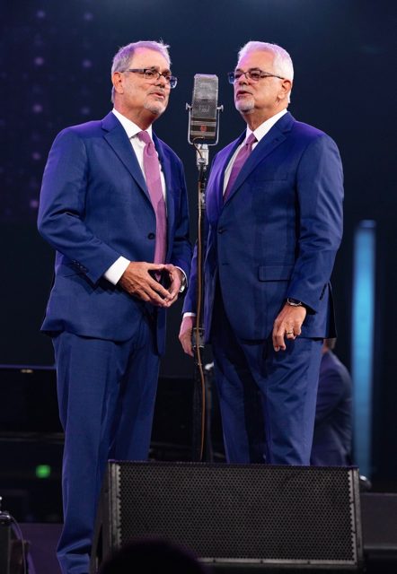 Two members of the Wills Brothers Quartet singing around a vintage microphone on the NQC MainStage